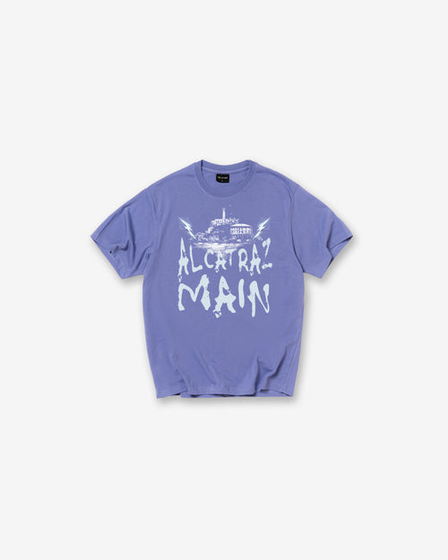 An Iris blue short-sleeve t-shirt with a white graphic print on the front reading 'ALCIRAZ MAIN' in a stylized font, displayed flat against a light gray background.